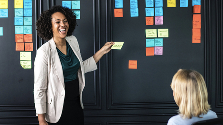 A woman holding a post-it note in front of a wall with lots of post-it notes on it.